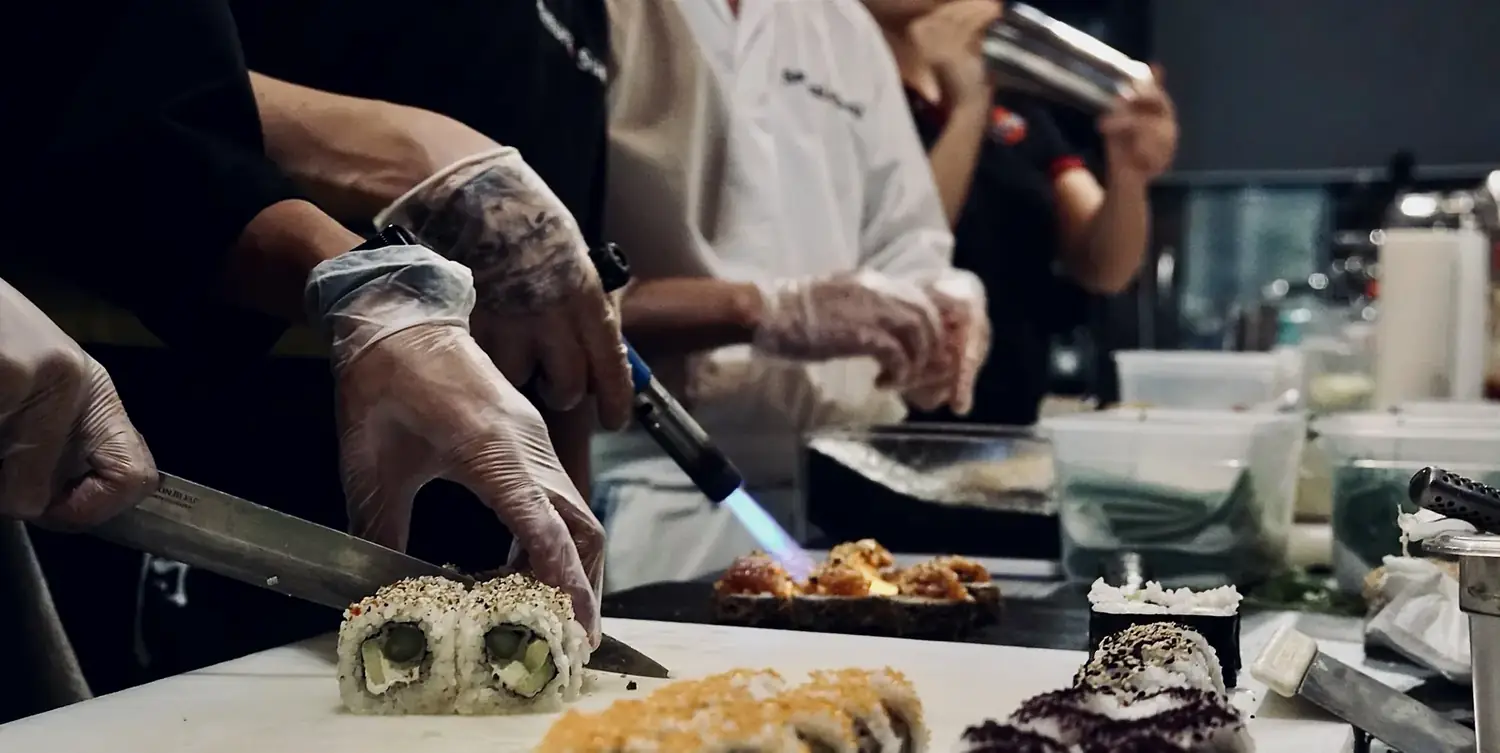 Hände schneiden eine frisch gerollte Sushi-Rolle